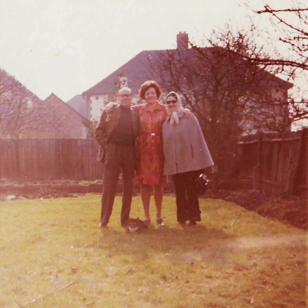 Nick Roth, Rucky van Mill and Caroline Salzedo standing in a garden, arms round each other, smiling at the camera
