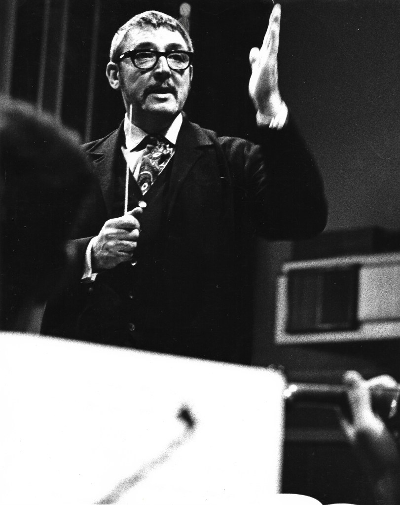 Black and white photo, man with glasses and moustache conducting an orchestra