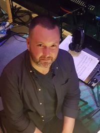 Photo of man looking up at camera with music and a keyboard behind him.