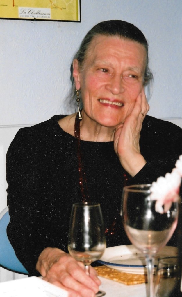 Woman smiling, wine glass on table in front of her, her hand on her cheek