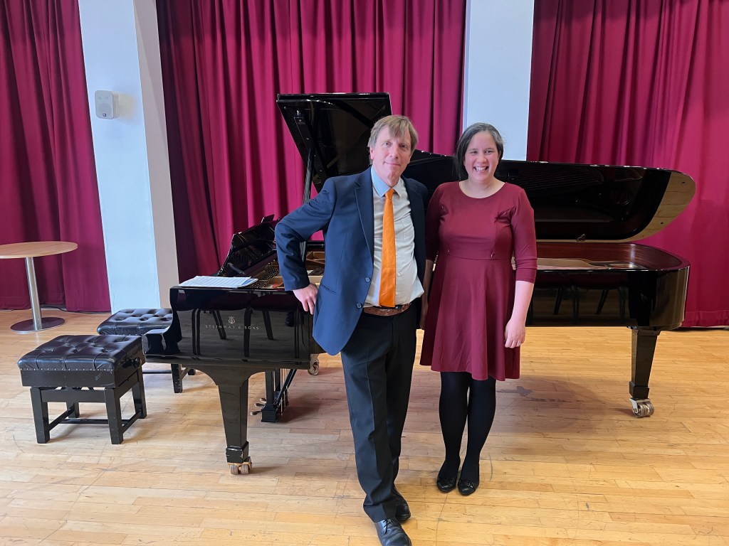 Man and woman standing in front of a grand piano smiling