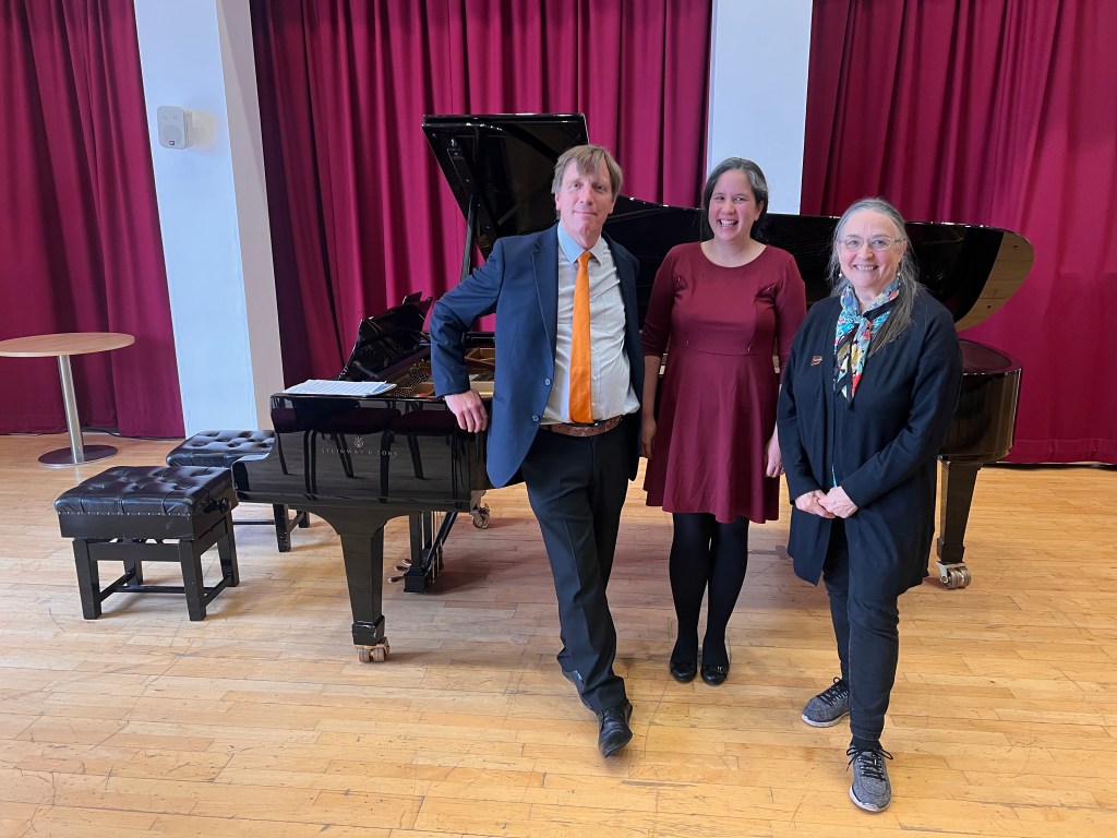 Man and two women standing in front of a grand piano, smiling